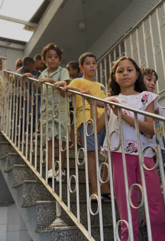 Crianças esperam em fila apoiadas no corrimão de uma escada