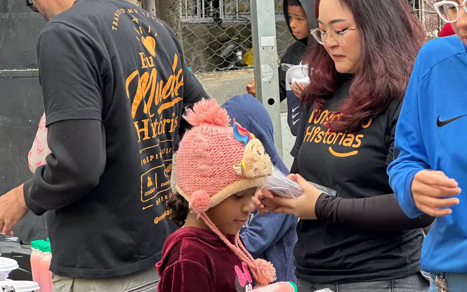 Colaboradores de camiseta da Mudando Histórias entregam refeições para uma criança em uma ação de rua